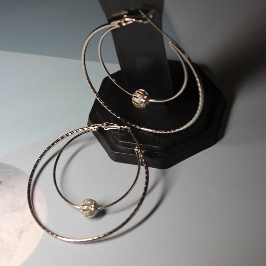 A pair of silver-colored hoops with beads. The hoops are circular in shape and made of shiny silver metal. Each hoop is adorned with multiple small beads, which are arranged in a symmetrical pattern. The beads vary in color and size, adding a vibrant and playful touch to the hoops. The silver color of the hoops creates a sleek and elegant appearance. The image showcases the intricate details of the beads and the smooth texture of the silver hoops.
